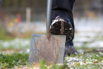 Booted foot pushing spade into ground
