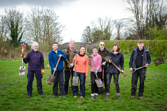 A group of volunteers pose for the camera in a park after planting a new community orchard.
