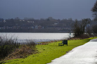 Park bench on grass next to a path, adjacent to the River Mersey