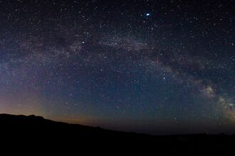 A spectacular view of the milky way above dark hills. An orange glow can be seen just above the hills