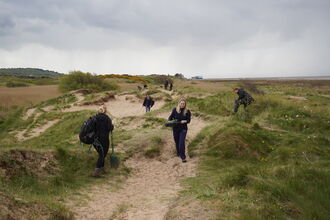 A number of conservation workers amongst dunes, carrying survey equipment etc.