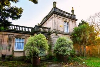 A castle like, listed building surrounded by trees and shrubs.
