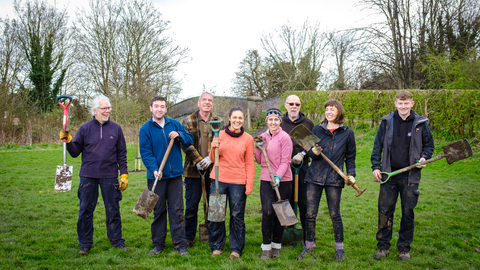 A group of volunteers pose for the camera in a park after planting a new community orchard.