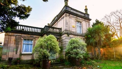 A castle like, listed building surrounded by trees and shrubs.