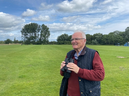 Brian smiles while holding his binoculars and looking out at the swifts above a park