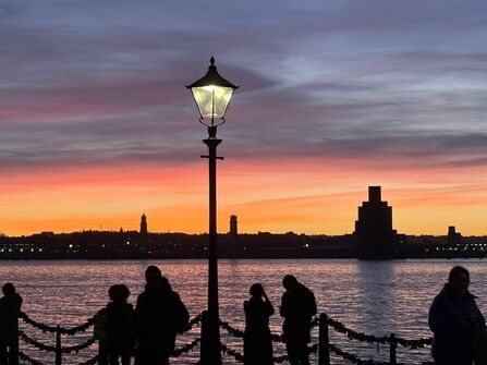 People looking out over the River Mersey at sunset